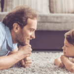 Adult male and little boy lying on carpet staring at each other