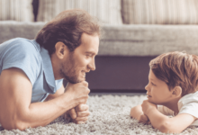 Adult male and little boy lying on carpet staring at each other