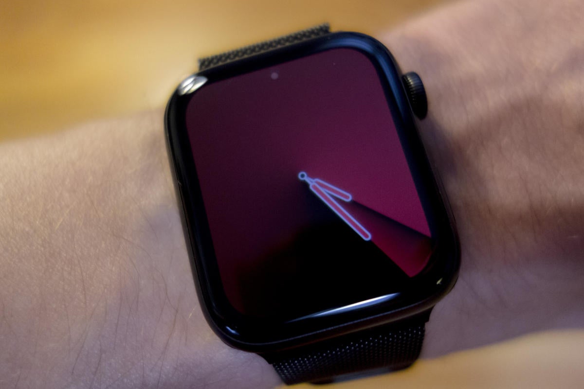 Un Apple Watch negro en la muñeca de una persona que muestra una cara degradada cónica de color morado oscuro.